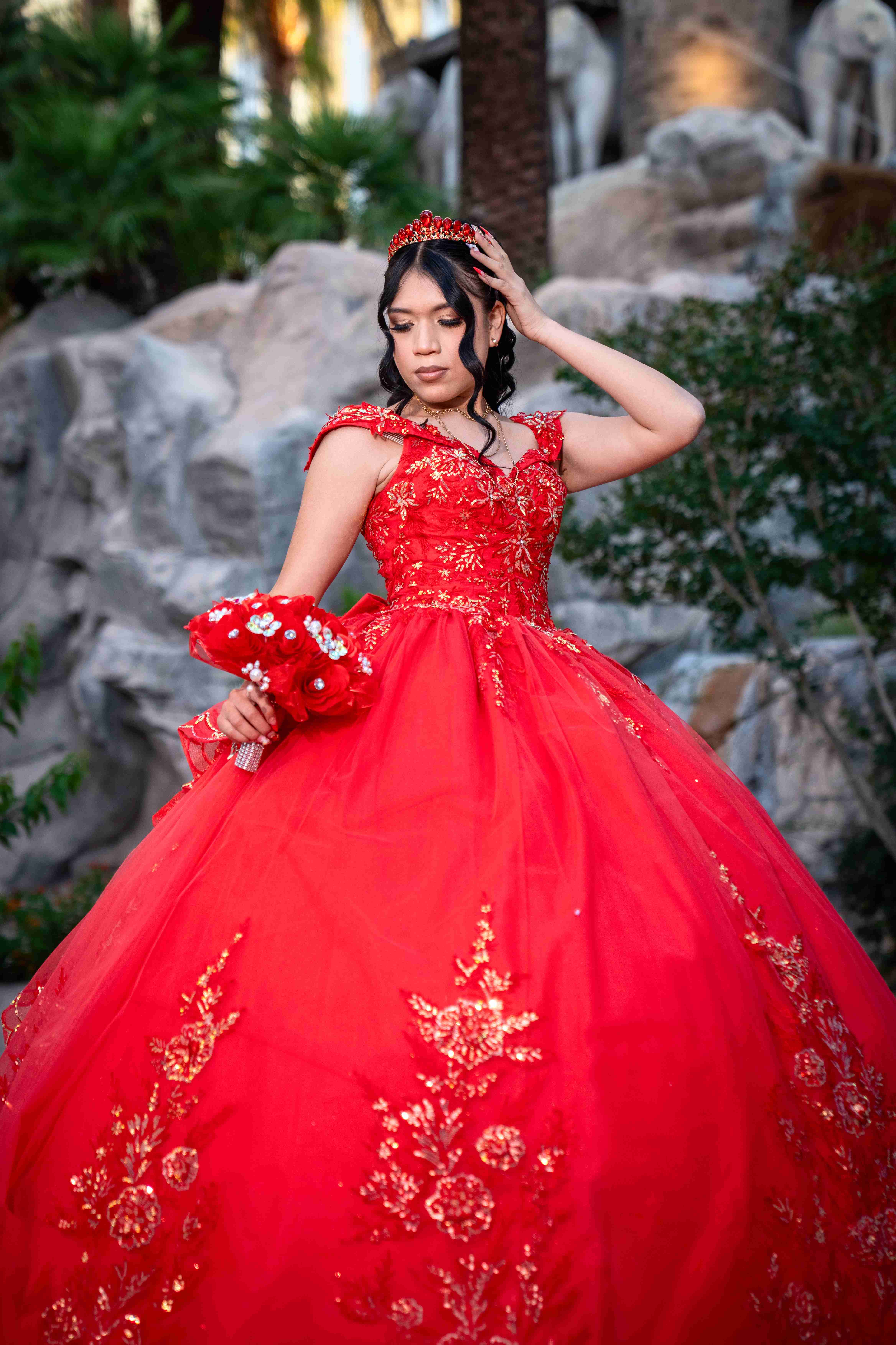 Quinceañera in red and gold gown at a rock garden